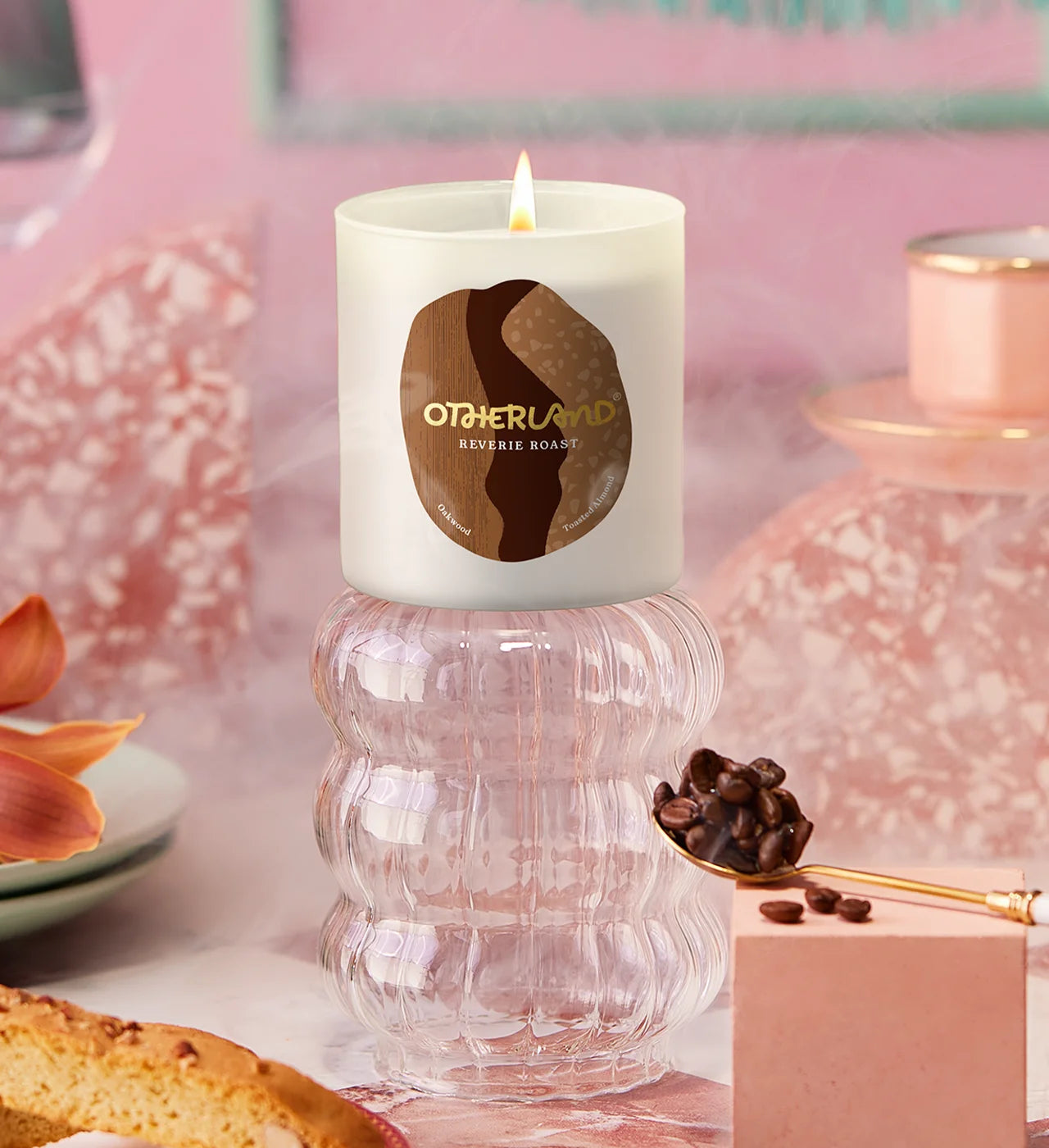Candle with Otherland on a decorative surface with coffee beans and pastries.