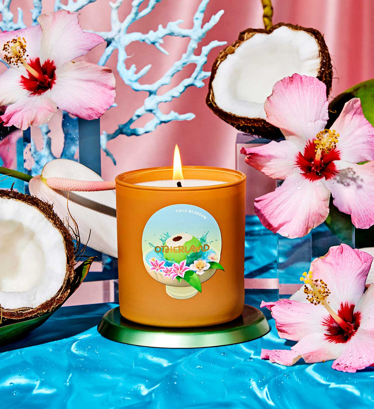 Candle with a floral label on a blue surface with pink flowers and coconuts.
