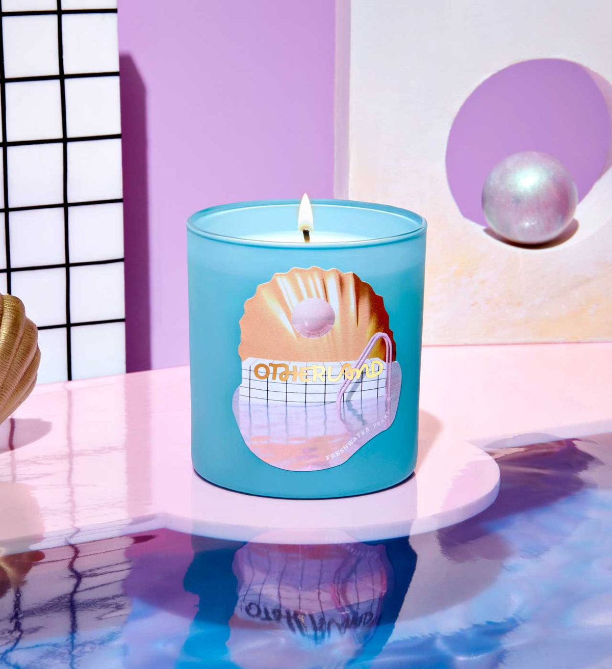 Blue candle with a shell design on a reflective surface with a pink and white background