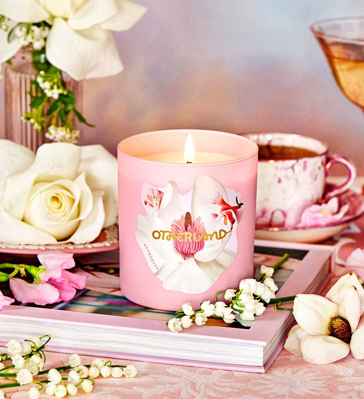 Pink candle with floral design on a table with flowers and a teacup.