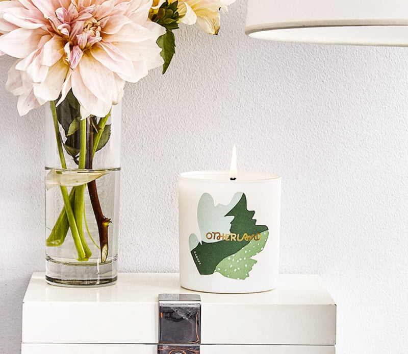 Lit candle on a nightstand next to a vase of flowers and lamp
