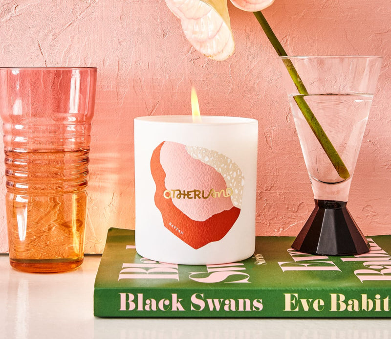 Lit Rattan candle on a nightstand next to a vase of flowers and a glass of water sitting on top of a book
