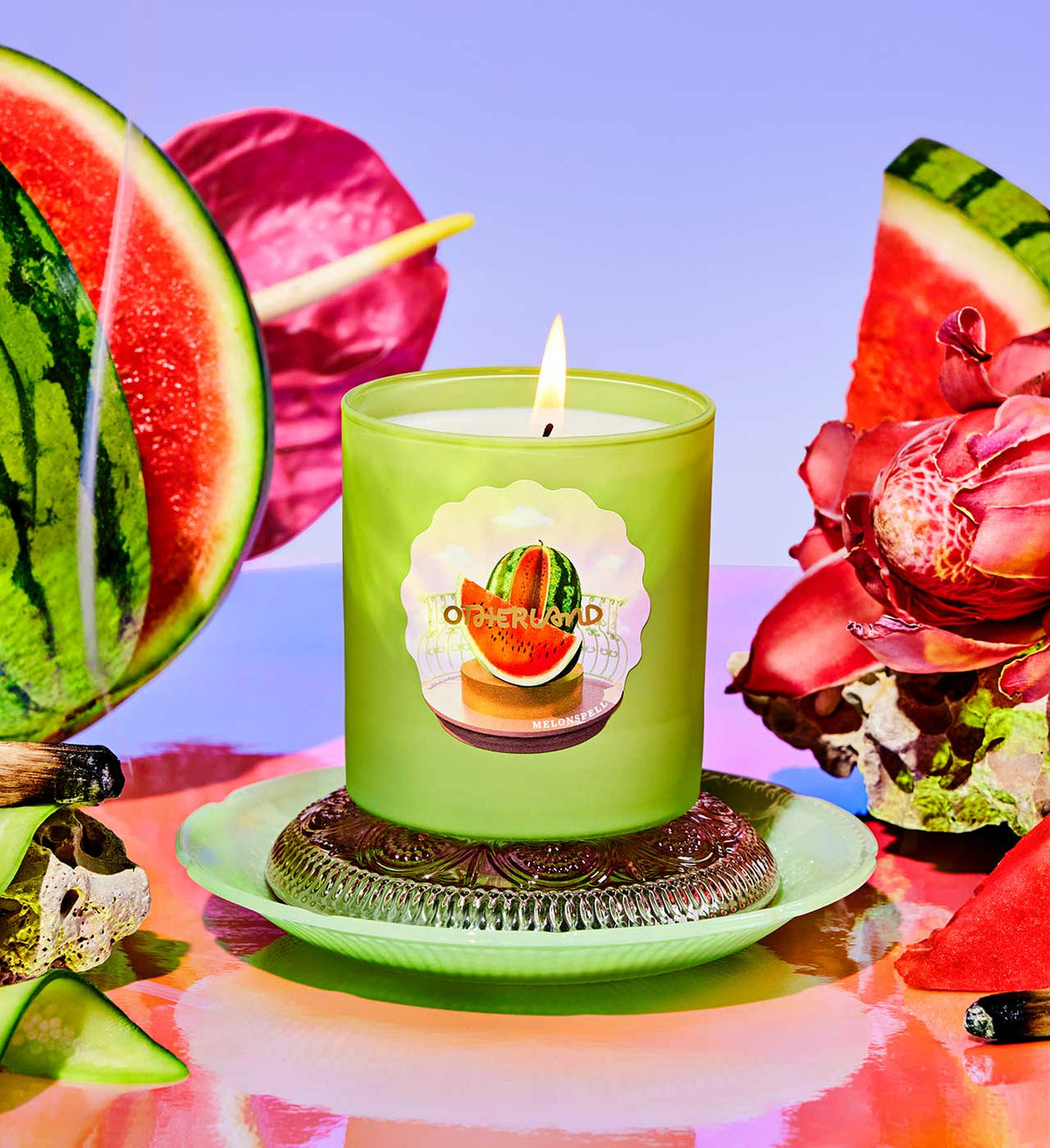 Green candle with watermelon design on a colorful background with watermelon slices and flowers.