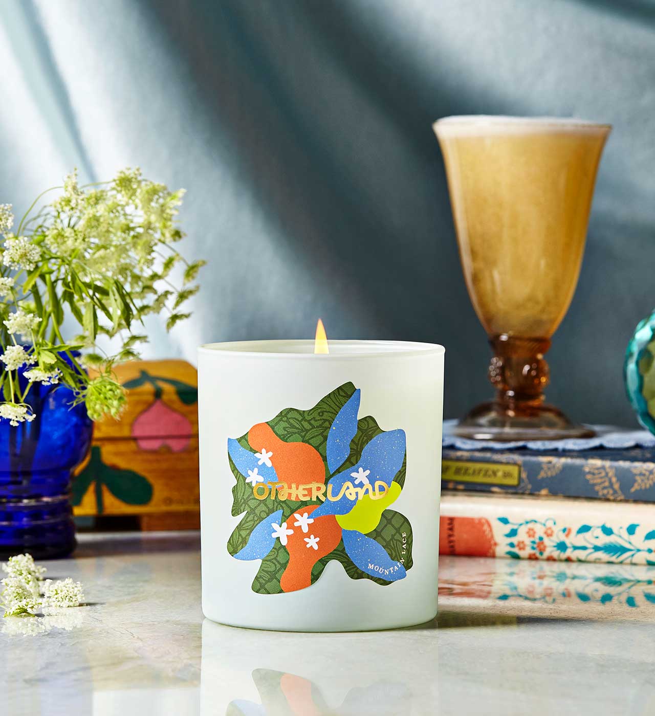 Candle with colorful design on a table with books and flowers