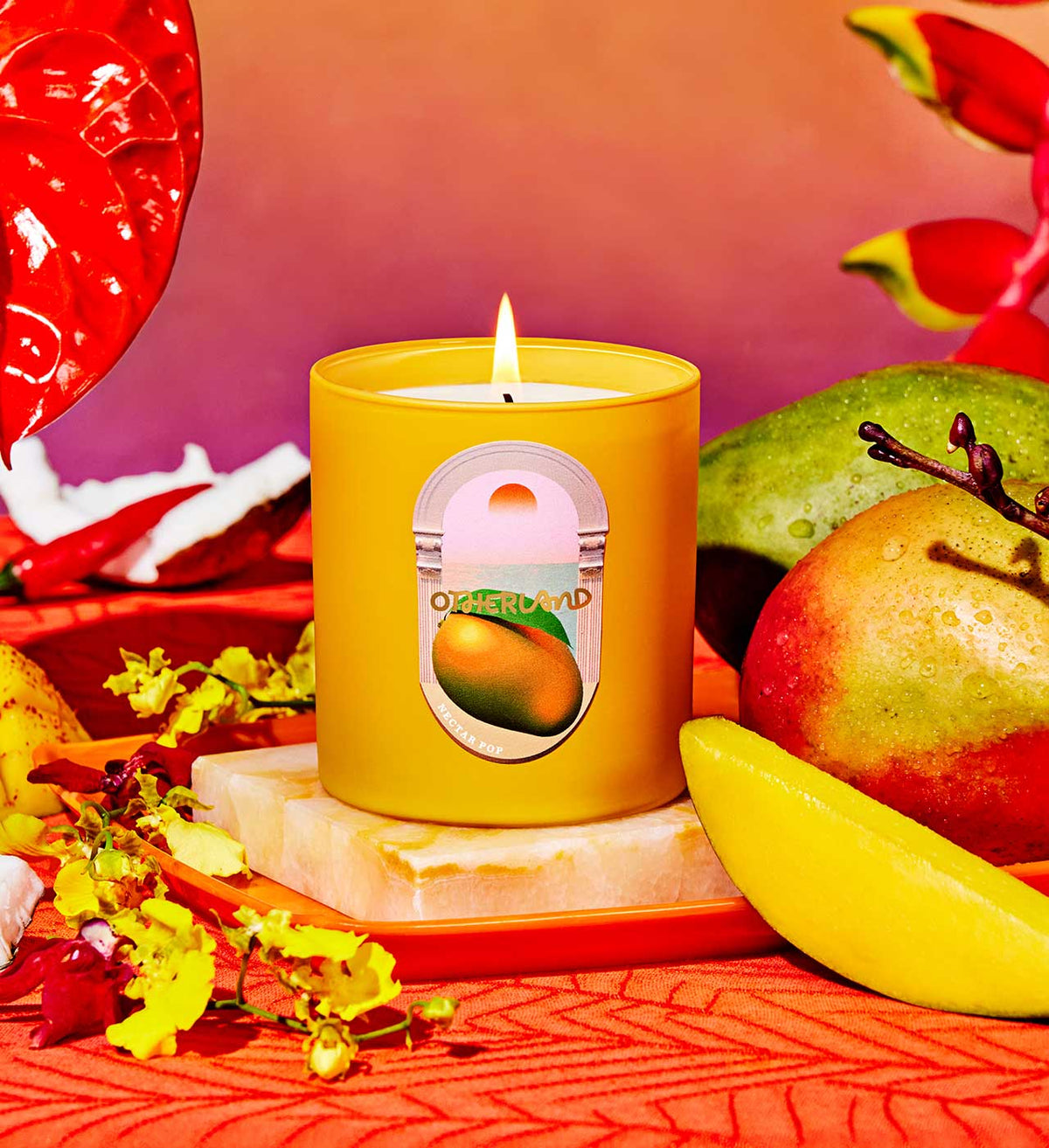 Yellow candle with a mango label on a decorative surface with fruits and flowers