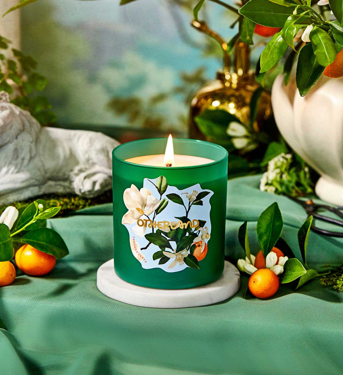 Green candle with floral design on a table with fruits and plants